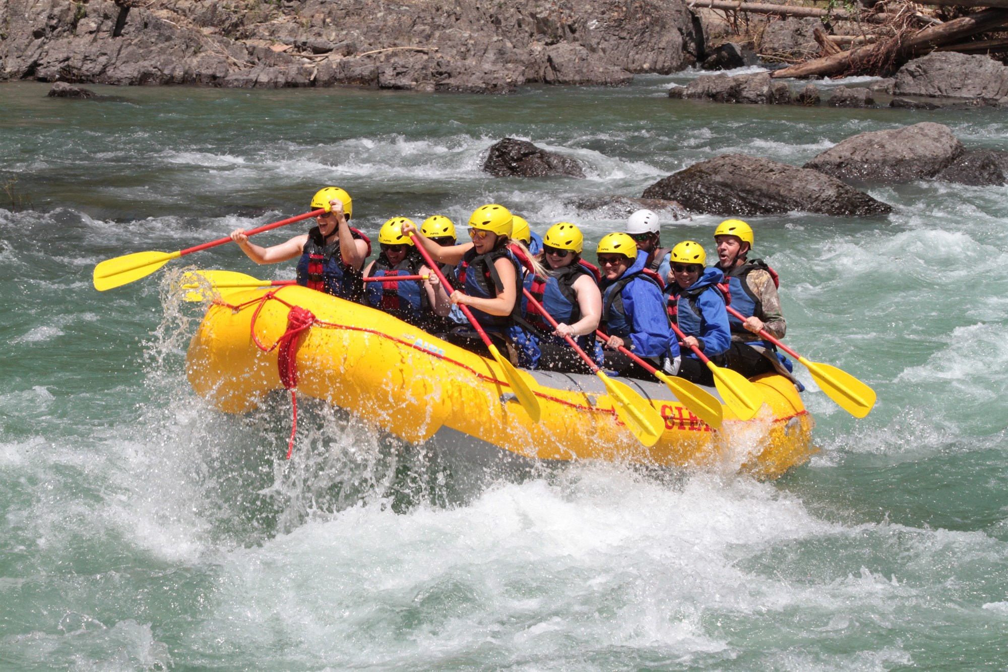 A group of people in a yellow raft navigating river rapids.