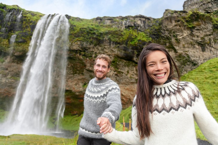 Iceland couple wearing Icelandic sweaters by Seljalandsfoss waterfall.