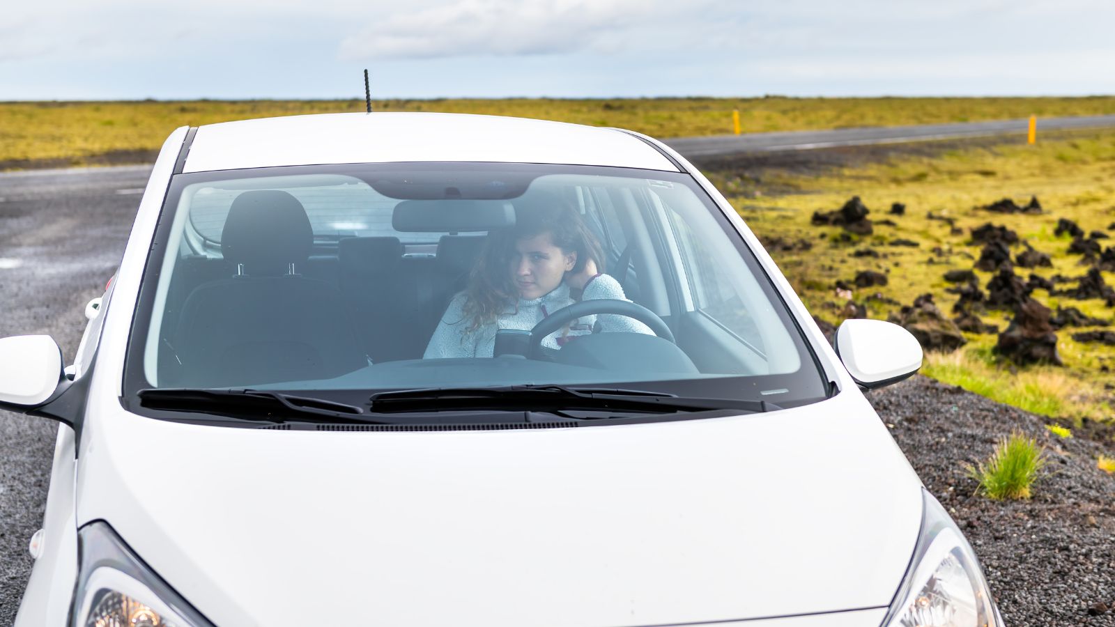 A  woman parking a small white Hyundai i10 smart car in a car park by the Ring Road in Laufskalavarda, South Iceland.