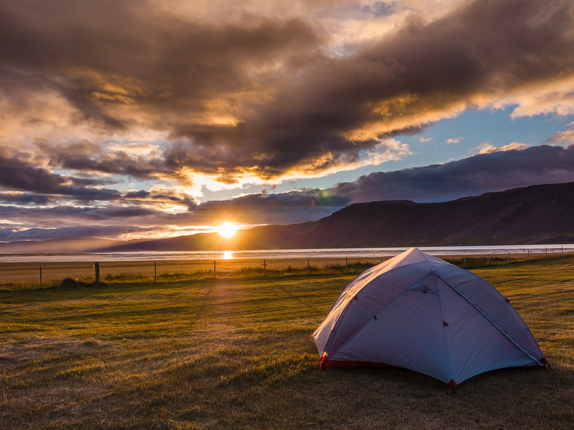 Tent pitched in Icelandic field as the sun rises over the rocky horizon.