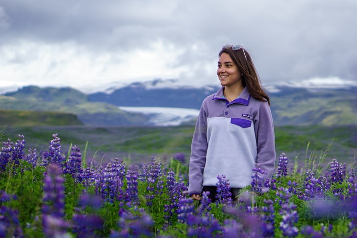 Woman standing in purple lavender fields with dramatic Iceland scenery.