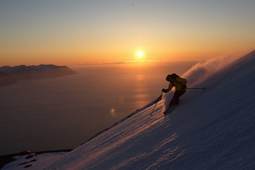 Person skiing down a steep slope with a sunset over the horizon.