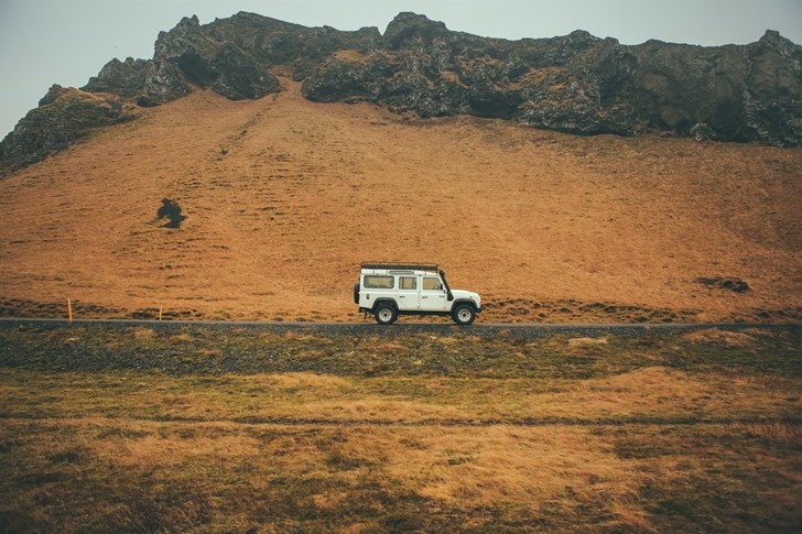 A white 4x4 car driving over rocky Iceland terrain.